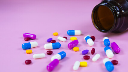 Multi-colored pills, capsules used in medical treatment are scattered on a pink background. Colorful pills, capsules and brown medicine bottle. Healthcare and medical concept. Space for text.