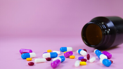 Multi-colored pills, capsules used in medical treatment are scattered on a pink background. Colorful pills, capsules and brown medicine bottle. Healthcare and medical concept. Space for text.