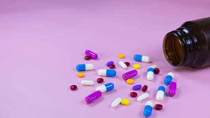 Multi-colored pills, capsules used in medical treatment are scattered on a pink background. Colorful pills, capsules and brown medicine bottle. Healthcare and medical concept. Space for text.