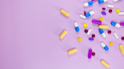 Multi-colored pills and capsules used in medical treatment are scattered on a pink background. Colorful pills and capsules. Healthcare and medical concept. Space for text.