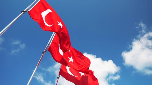 Slow motion of the row of Turkey national flags on high flagpole waving in the wind against a clear blue sky