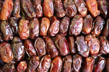 A close-up image of a pile of dates. The dates are a dark brown color and have a wrinkled texture..
