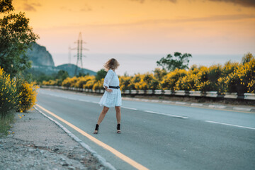 A woman in a white dress is standing on the side of a road