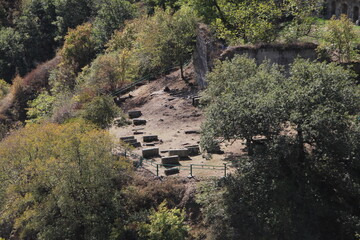 Ancient site with stone ruins, lush greenery, walls, columns, large stone altar on hillside....