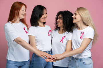 Diverse women joining hands showing pink ribbons for breast cancer awareness