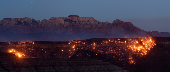 Hot spots in a partly contained wildfire burning above the Kolob Terrace road in Virgin, Utah, USA on July 27th 2024, glow under a twilight sky in front of West Temple Mountain as smoke drifts upward