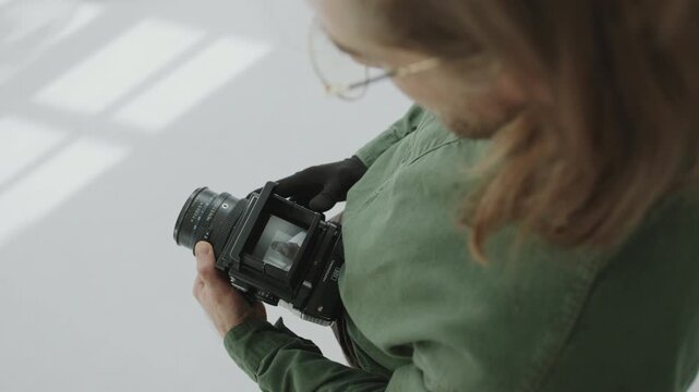 Photographer examining portraits of female model through viewfinder of medium format camera after studio photo shoot. Over the shoulder view