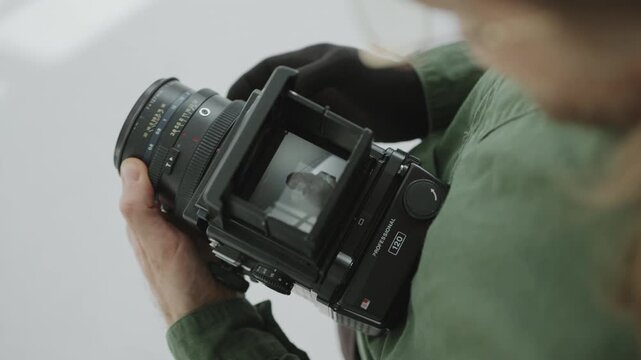 Photographer in glove checking studio photos of beautiful female model through viewfinder of medium format camera. Close-up view