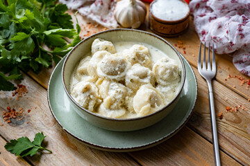 Dumplings with meat in cream sauce in a beautiful plate on a wooden table. Close-up. Ravioli with meat for lunch.