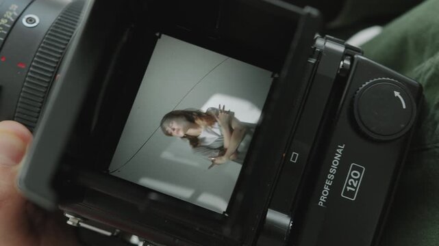 Hands of unrecognizable photographer reviewing photos of attractive female model on viewfinder of medium format camera. Close-up shot