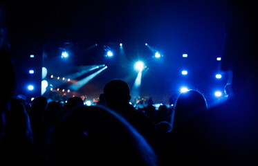 Silhouettes of spectators against a background of blue light at a concert