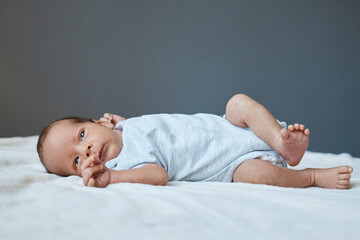 Little newborn baby boy lying on bed in the nursery wearing kid's clothes playing alone on white sheet copy space for promotion or commercial advertisement