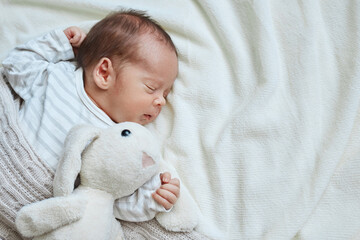 Peaceful newborn baby lying on bed sleeping on white sheets with soft rabbit infant child resting empty space for advertising