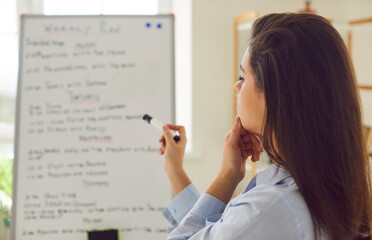 Focused woman, immersed in creating a event plan or schedule for the week on a whiteboard. The image captures the essence of strategic work, organization timeline, and meticulous planning agenda.