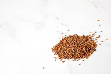 Close view of a heap of roasted buckwheat grains on white marble tabletop with copy space