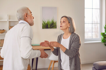Upset senior couple quarreling in the living room at home. Unhappy elderly man and woman arguing with each other having problems in relationships. Marriage quarrel, and divorce concept.