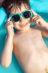 cute boy kid in inflatable pool with sunglasses on eyes or head. child is having fun lying in water, gets tan.smiling preschooler in summer vacation.