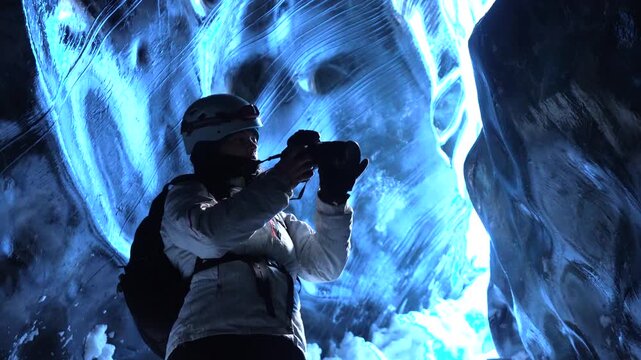 Female photographer taking pictures in the ice cave, Vatnajokull glacier, Hvannadalshnukur, Iceland next to Jokulsarlon