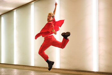 Young man with dyed hair and red clothes is dancing urban dance in a illuminated hallway