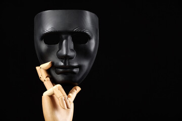 Wooden mannequin hand holding plastic mask on black background, space for text. Theatrical...