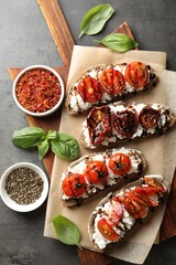 Delicious ricotta bruschettas with sun dried tomatoes, spices and basil on grey textured table, flat lay