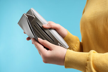 Woman with empty wallet on light blue background, closeup