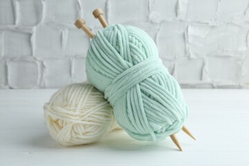 Skeins of yarn and knitting needles on white wooden table, closeup
