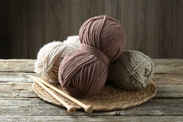 Skeins of yarn, knitting needles and wicker mat on wooden table, closeup