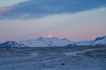 Moon behind the mountains on frozen Solheimasandur beach in winter with snow in Iceland