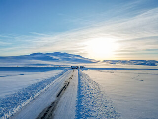 Aerial drone view. Frozen road in winter in Iceland. Snow-filled roadsides during winter with blue sky.
