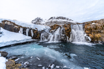 Frozen waterfall next to famous Kirkjufell mountain in Iceland winter