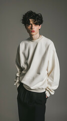 Obraz premium A young model with curly hair poses in a white sweater and dark pants against a plain background, showcasing a relaxed, modern style with a touch of elegance and urban chic