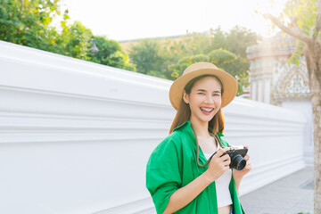 Young Asian woman traveler wearing green shirt with taking picture using a camera at temple. summer...