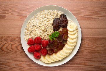 Delicious and healthy bowl of oatmeal with raspberries, dates, grapes and banana.
