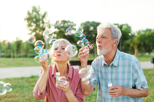 woman man senior couple together elderly active happy retirement bubble soap blowing fun blow vitality bonding park outdoor leisure park fun - Powered by Adobe