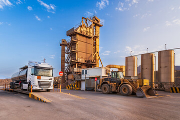 Asphalt production plant, with a tanker truck with bitumen on the scale, a loader and bitumen tanks.