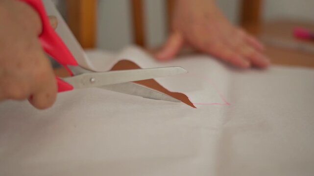 Close-up of a senior woman cutting fabric with scissors, preparing for a sewing project.