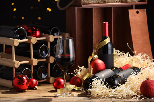 Bottles of wine, glass, wooden box, corks and red Christmas balls on table