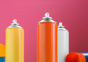 Many spray paint cans on pink background, closeup