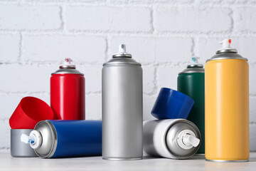 Cans of spray paint on wooden table near white brick wall