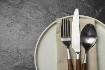 Stylish cutlery, plate and napkin on black table, top view. Space for text