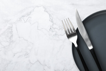 Stylish cutlery and plate on white marble table, top view. Space for text