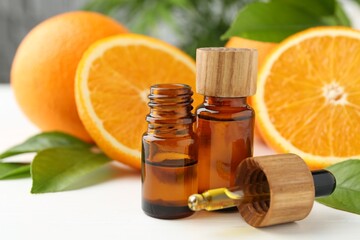 Essential oils in bottles, dropper, oranges and green leaves on white table, closeup