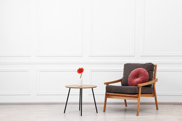 Fototapeta premium Comfortable armchair with pillow and coffee table near white wall, space for text. Interior design