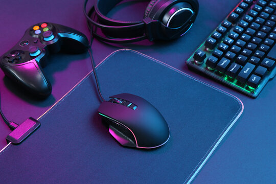 Computer mouse, RGB keyboard, game controller and headset in neon lights on dark background
