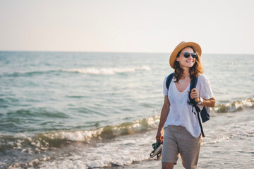 Young woman in a hat and sunglasses walking along the sea beach on a summer day