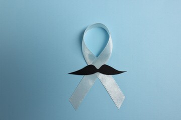 Light blue ribbon and fake mustache on color background, top view. Prostate cancer awareness
