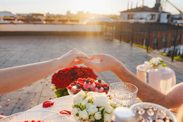 Romantic dinner on the rooftop at sunset. A couple is holding hands on the background of a table...