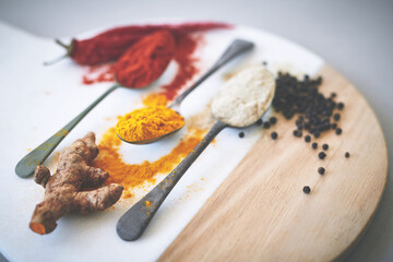 Board, turmeric and spoon in gray background for spices, curry and sensory appeal for creativity with culinary. Studio, condiment or seasoning for cooking with powder, aroma or ingredients collection