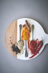 Board, spices and spoon in gray background for aroma, flavor and sensory appeal for creativity with culinary. Studio, condiment and seasoning for cooking with curry, powder and ingredients collection